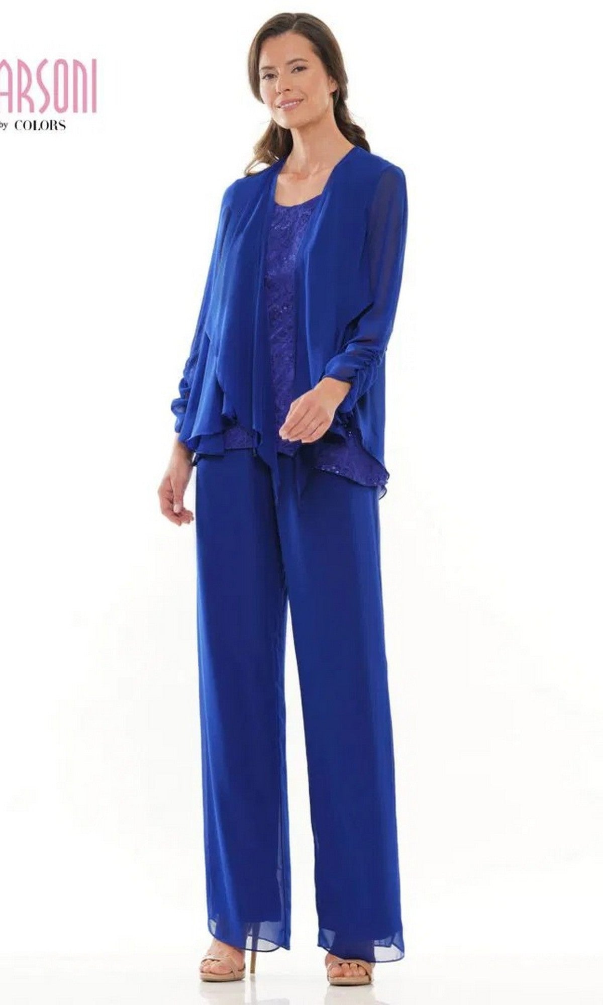 A woman smiles in the Marsoni M303 Long Formal Pantsuit in sapphire, featuring a layered chiffon jacket, sleeveless lace top, wide-leg trousers, and beige heels.